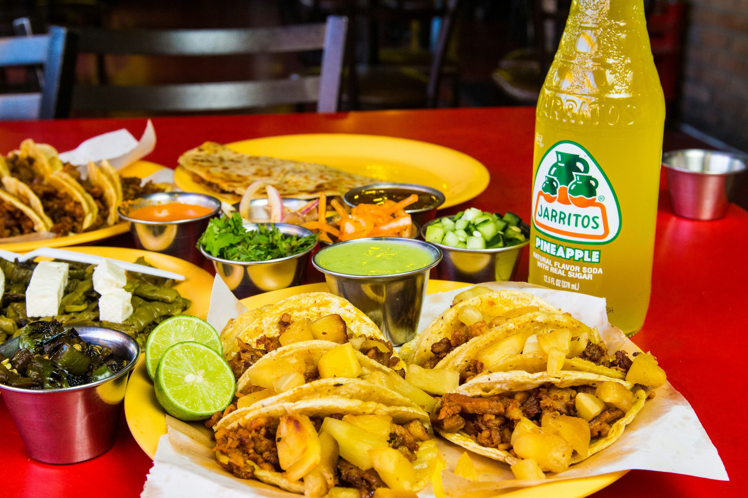 Tacos al pastor served with a bottle of pineapple Jarritos soda and sides