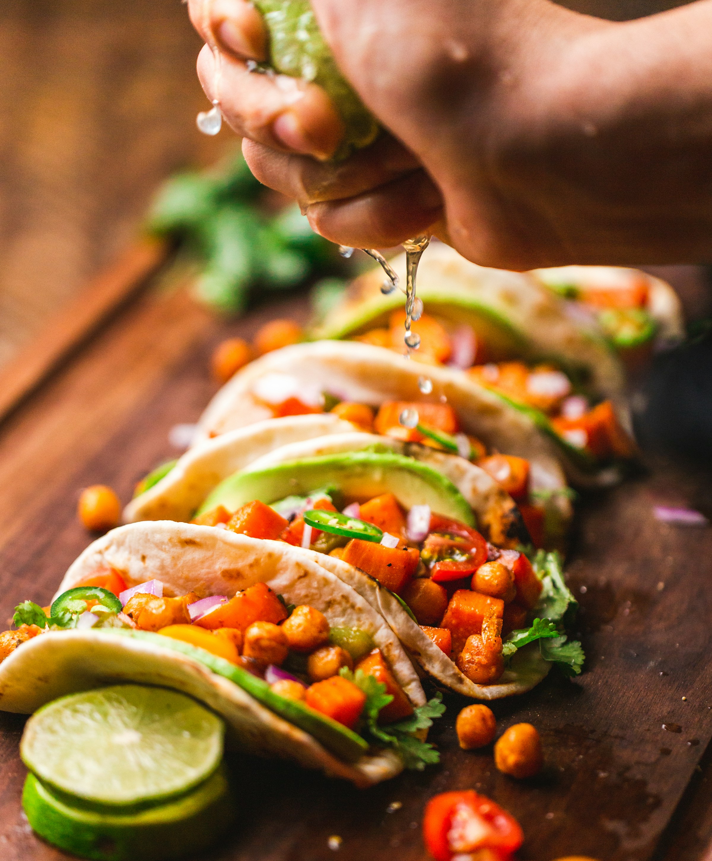 An assortment of tacos on a wooden plate with salsa and lime