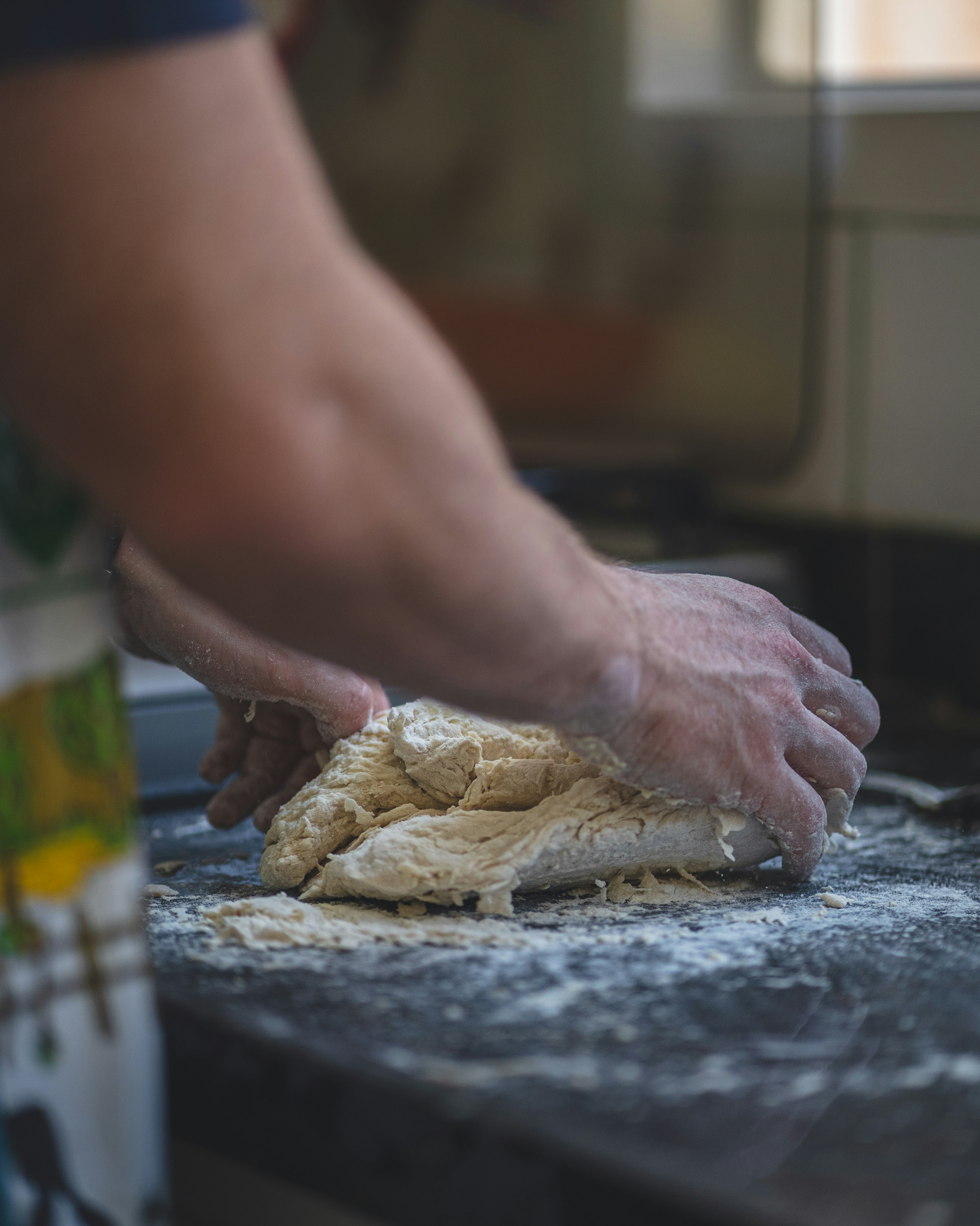 Hands stretching a round of dough on a floured bench.