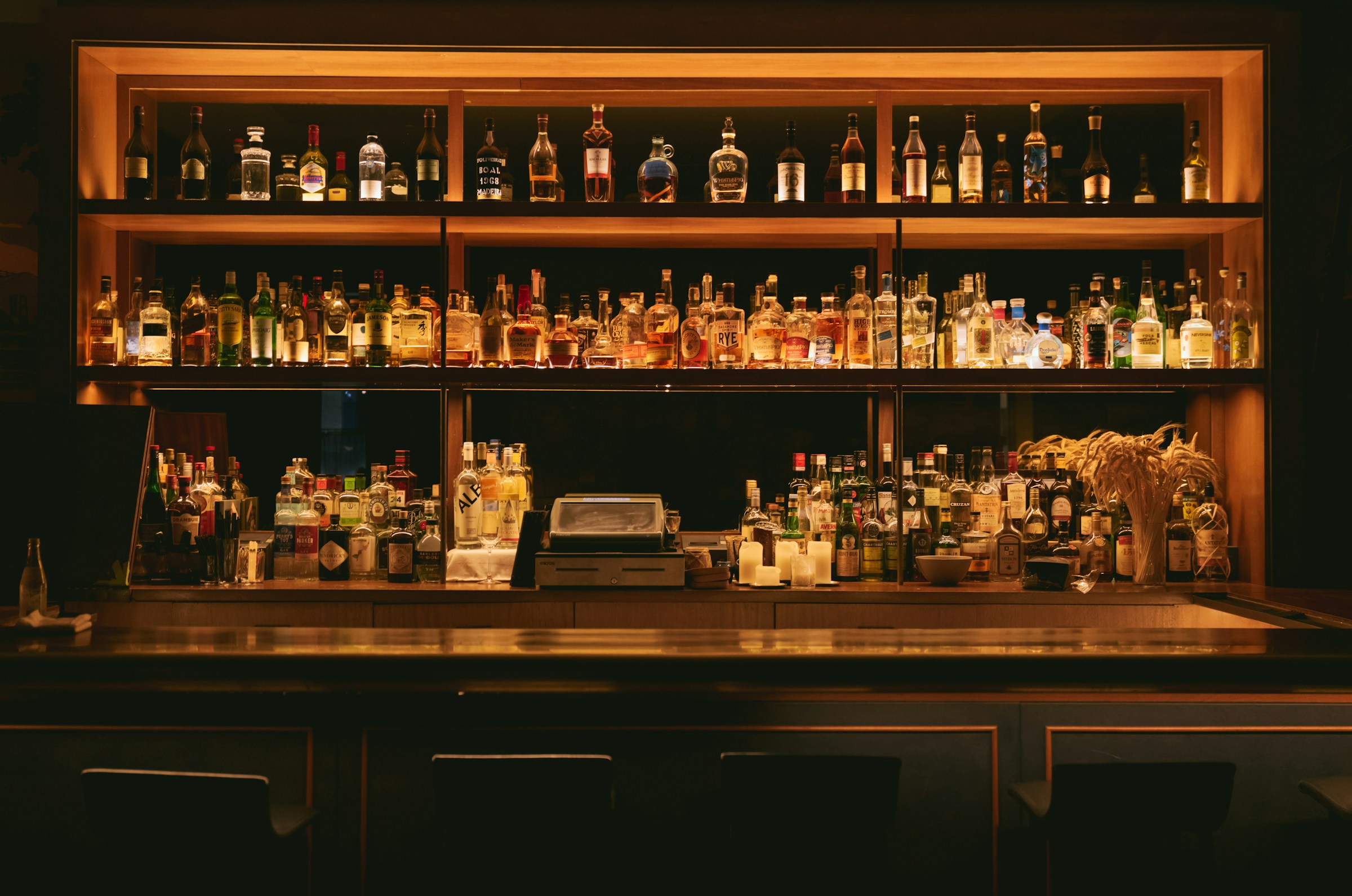 The back bar, shelves of spirits bottles warmly backlit above the well