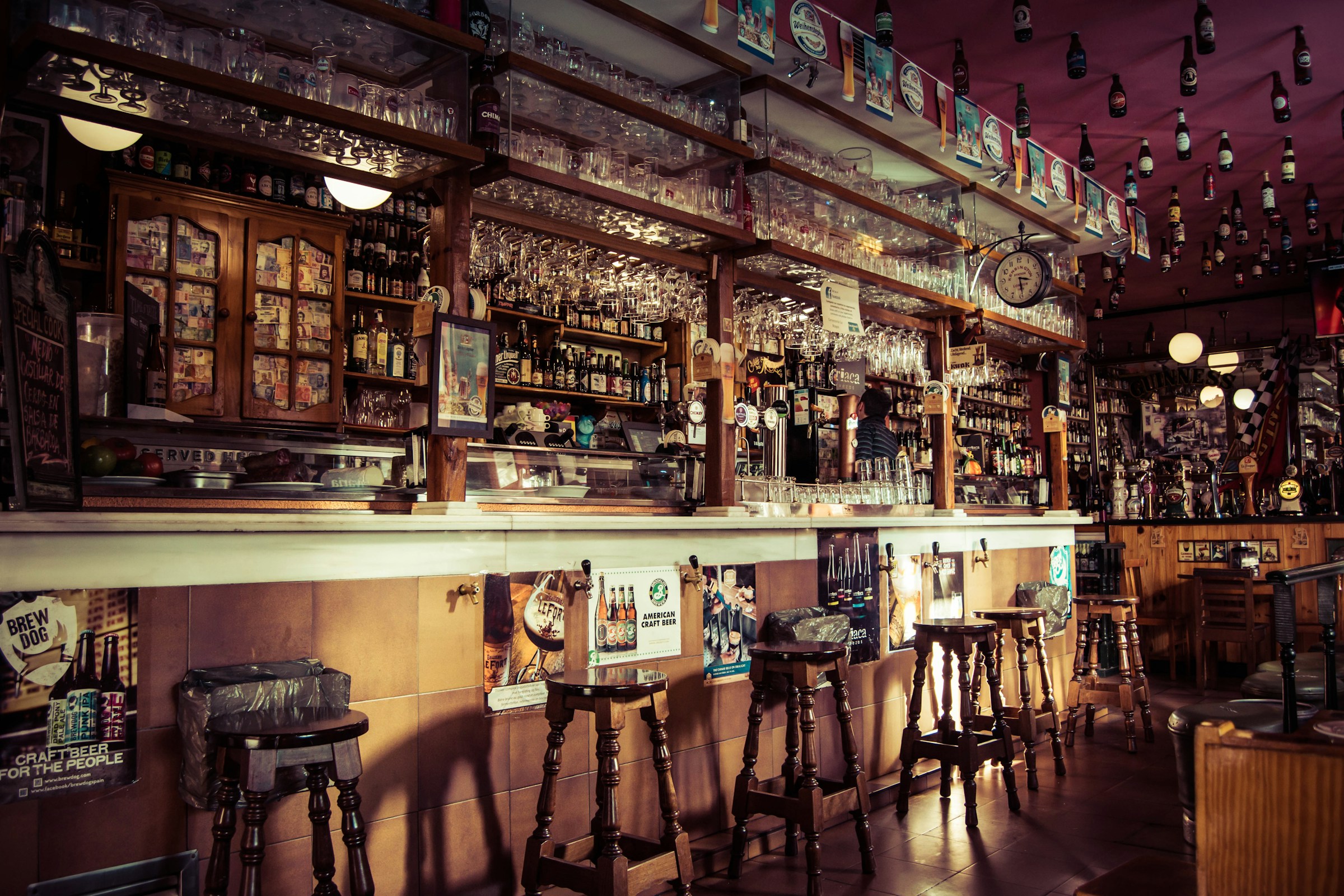 The main bar in warm light, wooden stools lined along the counter under racks of glassware and shelves of bottles