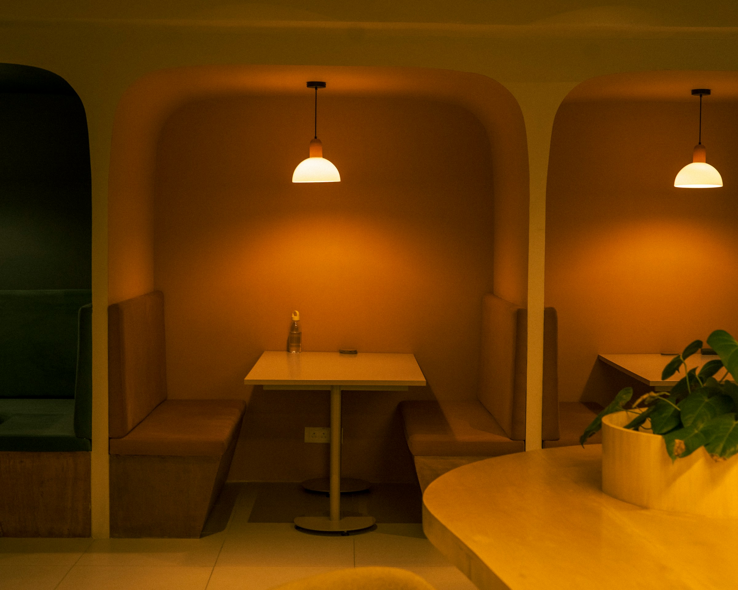A corner booth under a warm pendant lamp, upholstered benches around a small table