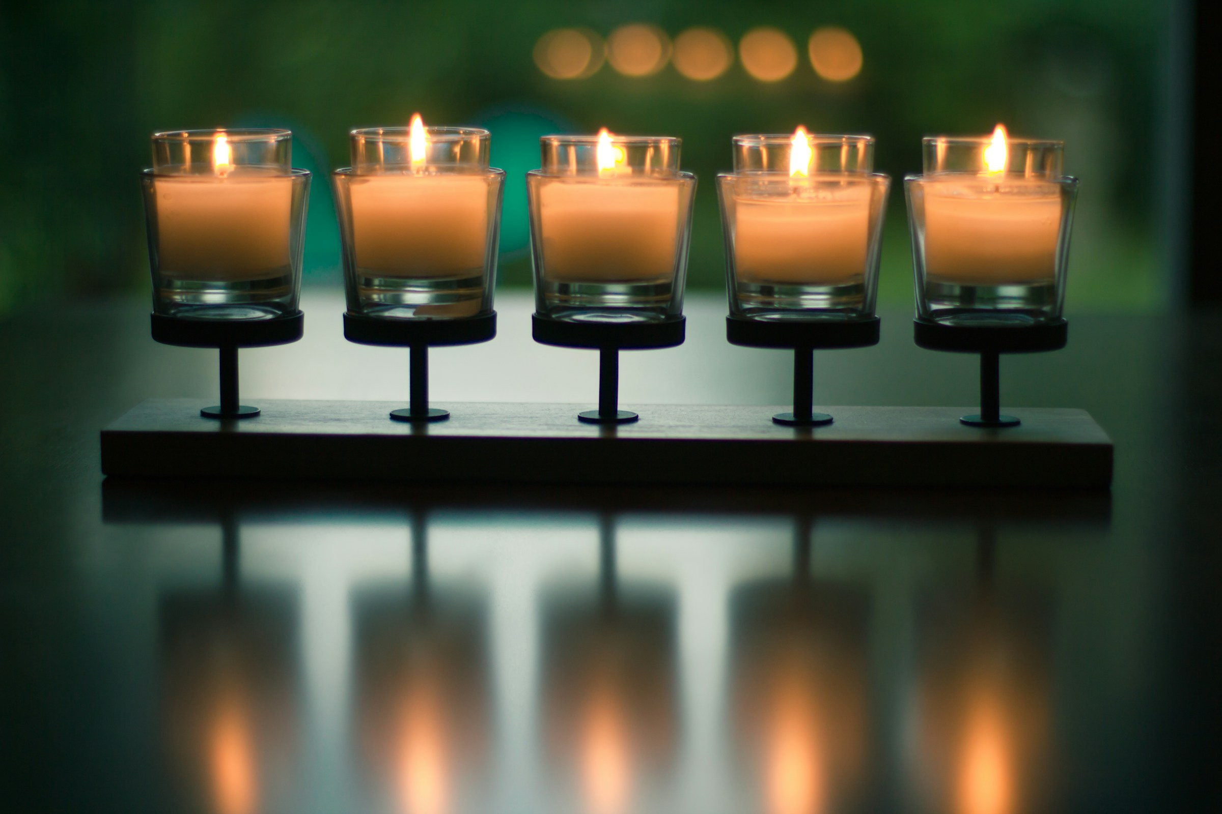 A row of five votive candles burning on a dark reflective surface